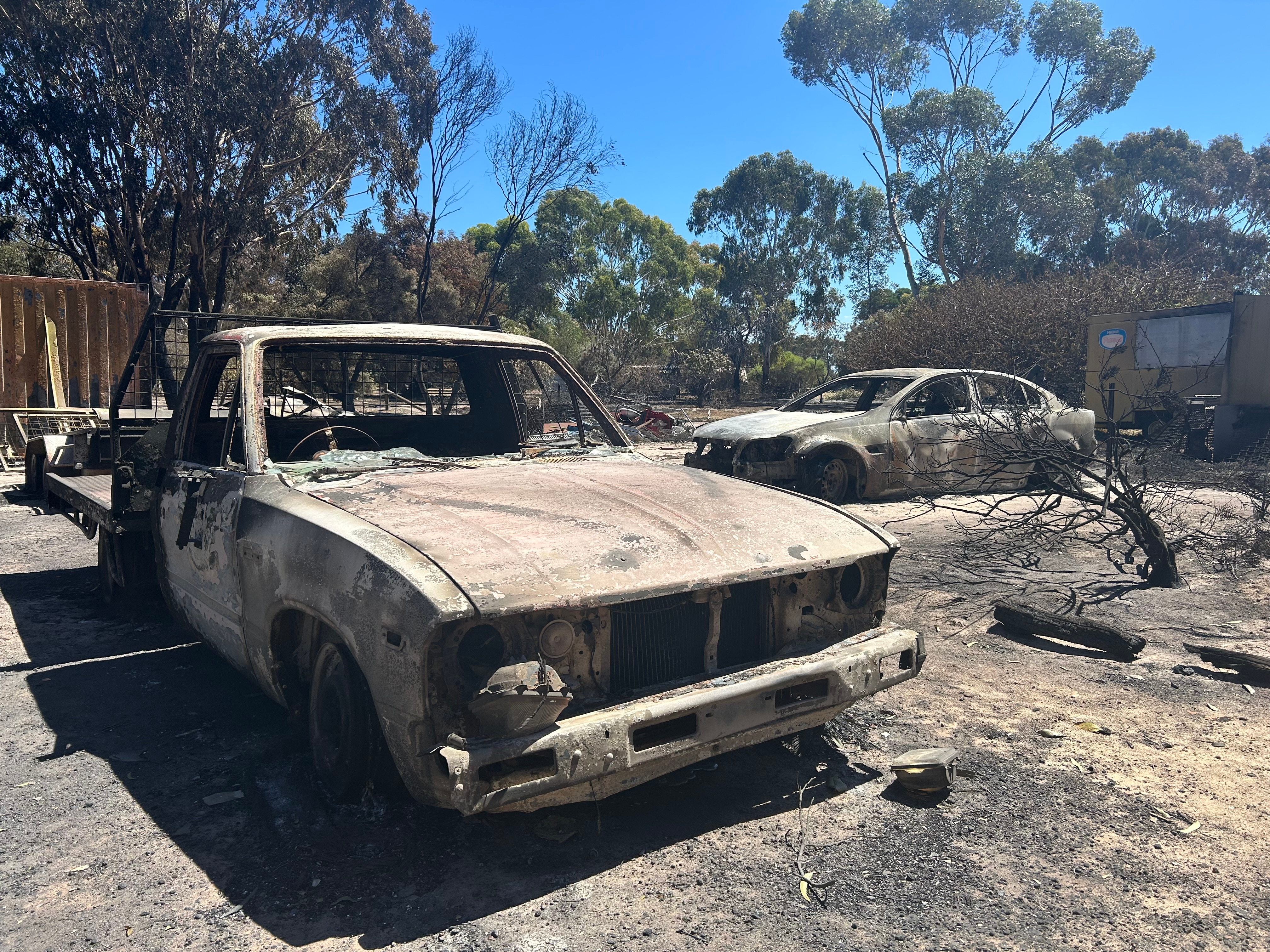The burntout shells of a ute and a sedan on a scorched property,