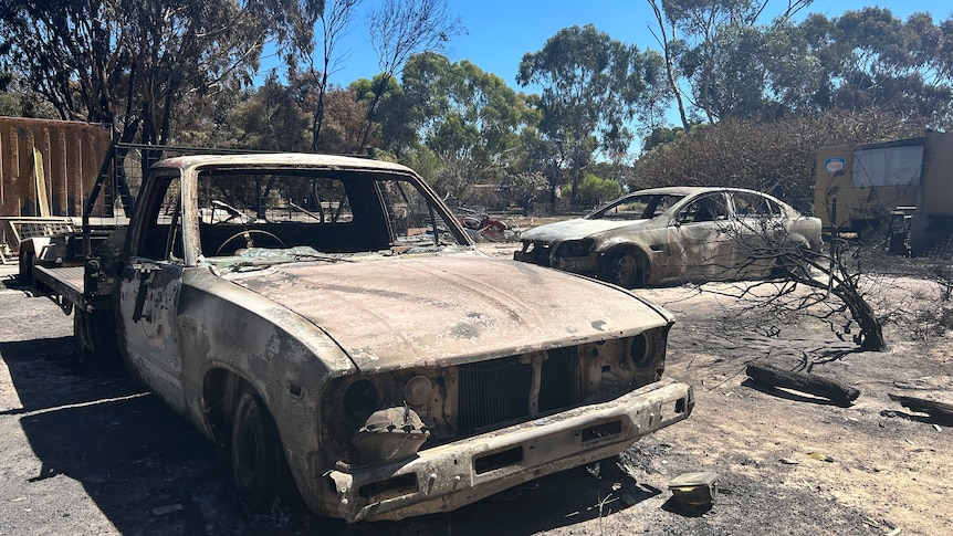 The burntout shells of a ute and a sedan on a scorched property,