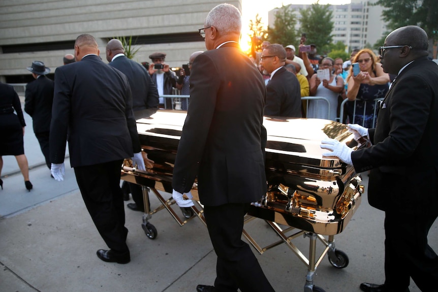 Four men in black suits carry Aretha Franklin's gold casket.
