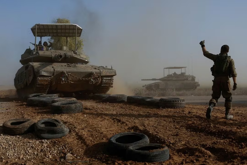 An Israeli soldier gestures towards a tank crew member as it crosses a road.
