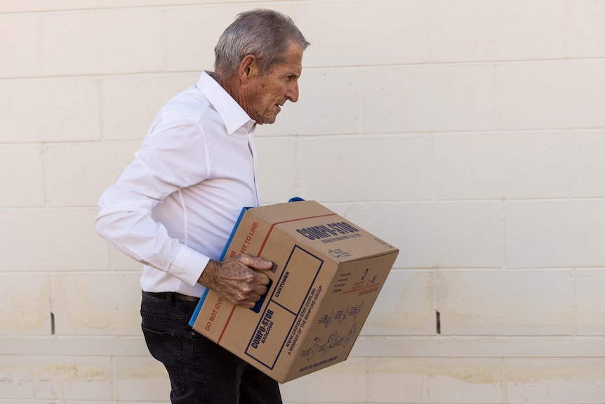 An elderly man carries a box as he leaves court.  