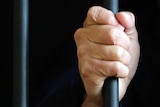 A prisoner holds onto a bar in his prison cell.