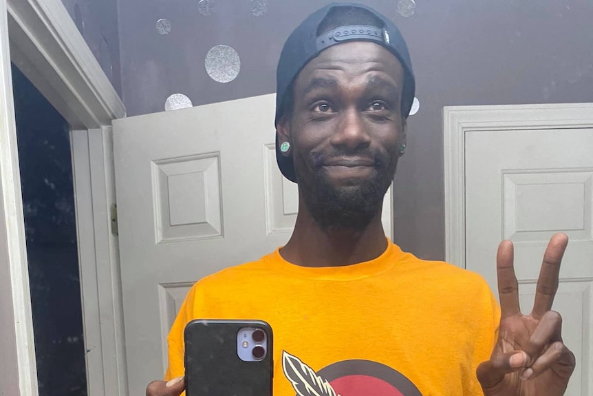 A young Black man gives a peace sign while taking a mirror selfie