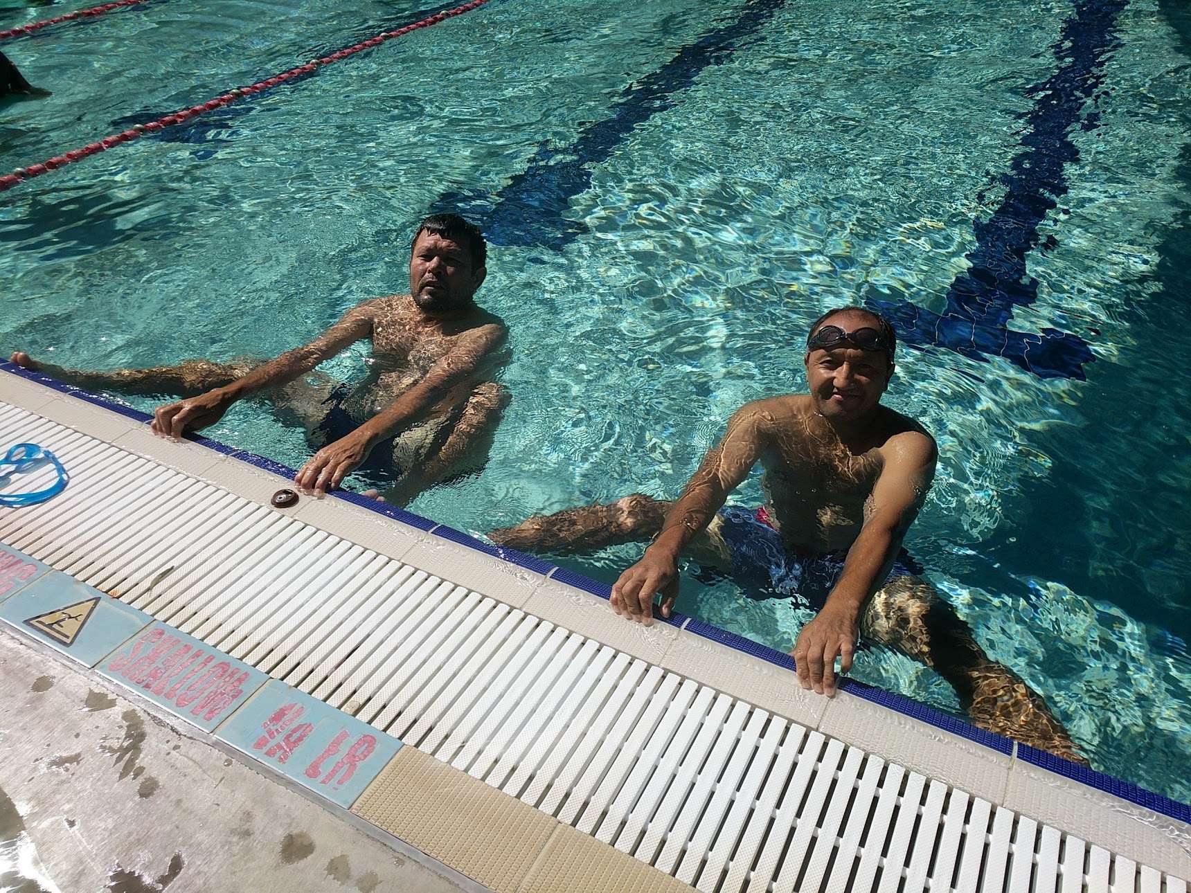 two men in a pool holding on to the pool edge smiling