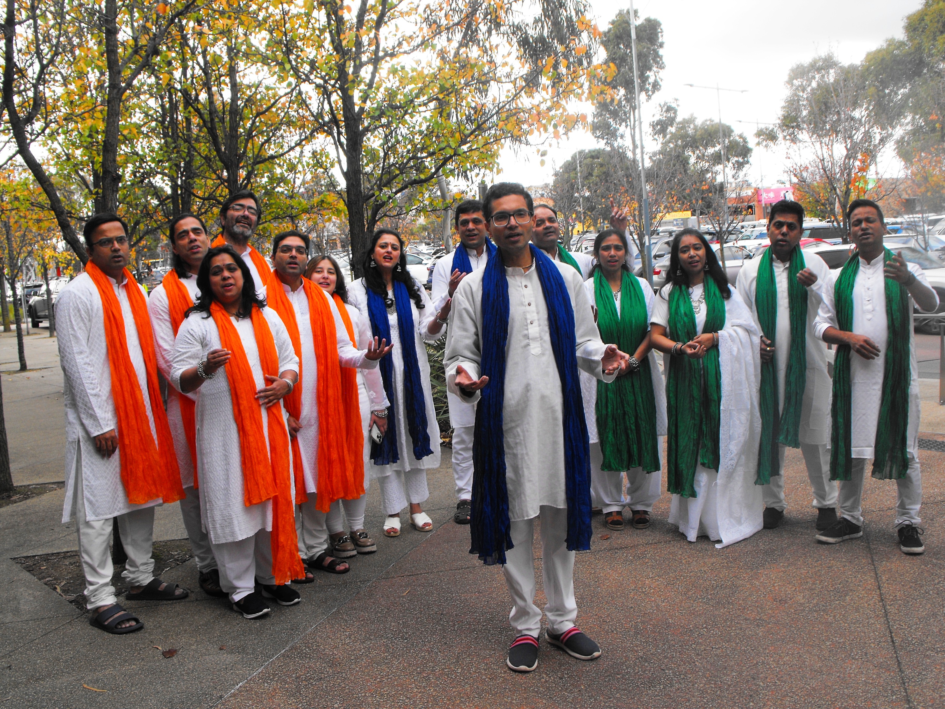 Viraj stands in front of men, women, sings, all wear kurta, white scarfs in the Indian tricolour saffron, green, white and blue.