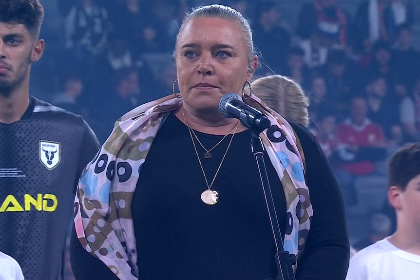 a woman standing behind a microphone and talking at a football match