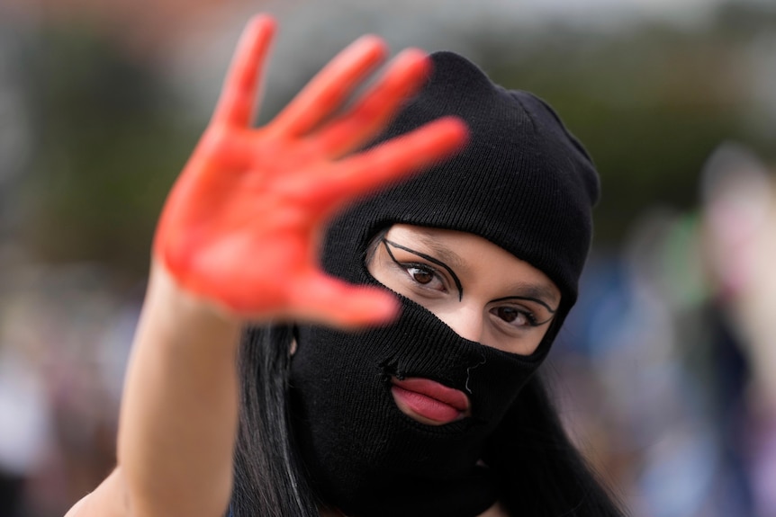 A masked woman holds her red stained hand up during a march marking International Women's Day.