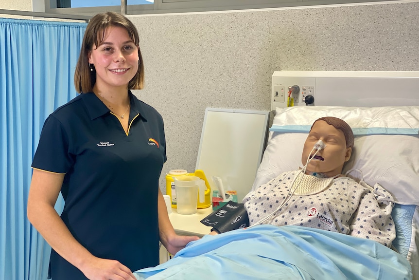 A woman in a nurse uniform, next to a hospital bed.