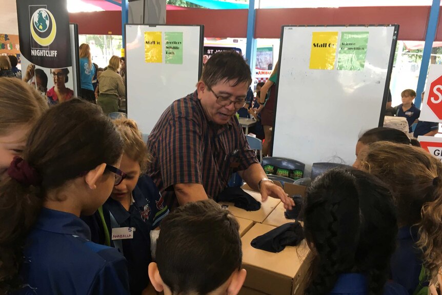 Retired science teacher John Rivas is surrounded by excited primary school children during an annual science exhibition.