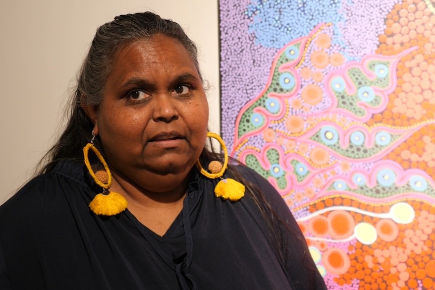 a woman looking off camera standing in front of a colorful painting 