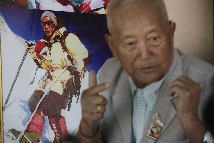 Mr Sherchan sitting next to a photograph of himself taken during his previous summit of Mount Everest.