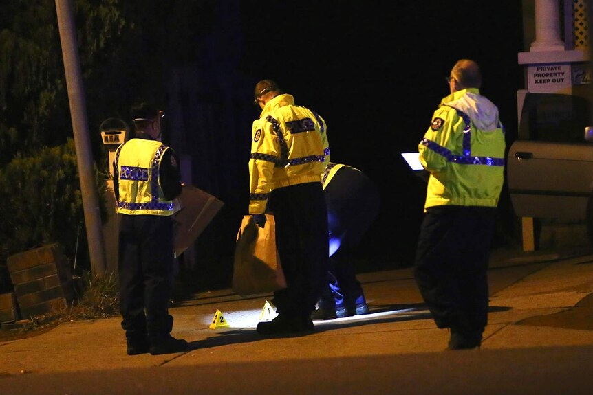 A wide shot showing four police officers in hi-vis clothing looking at something on the ground in a street.