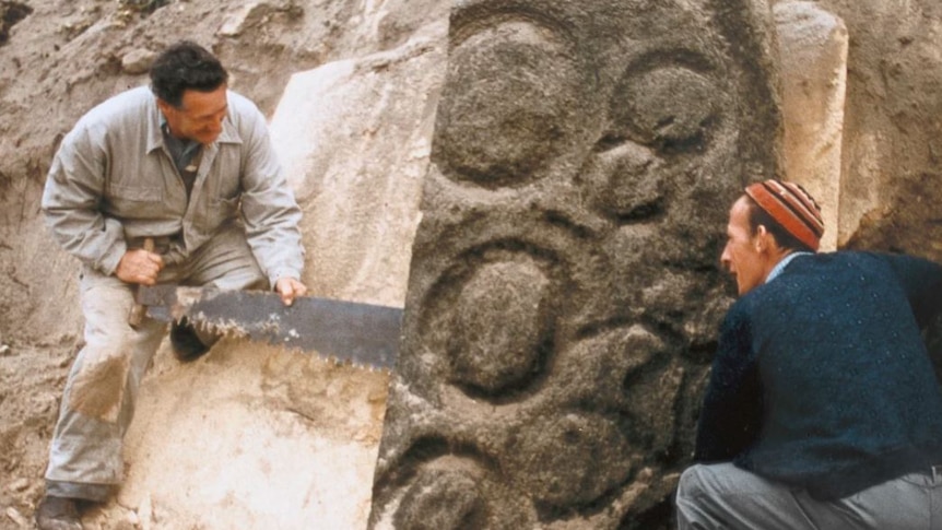 Two men sawing at a piece of rock art.