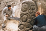 Two men sawing at a piece of rock art.