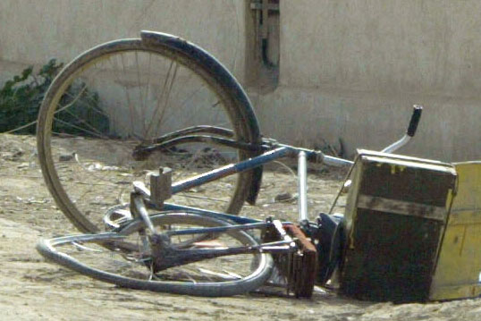 A blue bicycle lies on its side in street in Iraq.