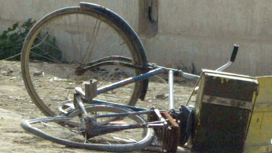 A blue bicycle lies on its side in street in Iraq.