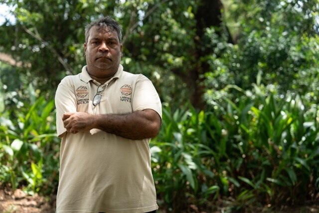 Man sits in front of trees being interviewed on camera by journalist