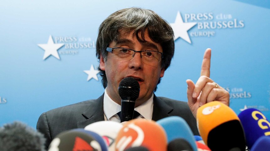 Sacked Catalan leader Carles Puigdemont speaks into microphones at a press conference.