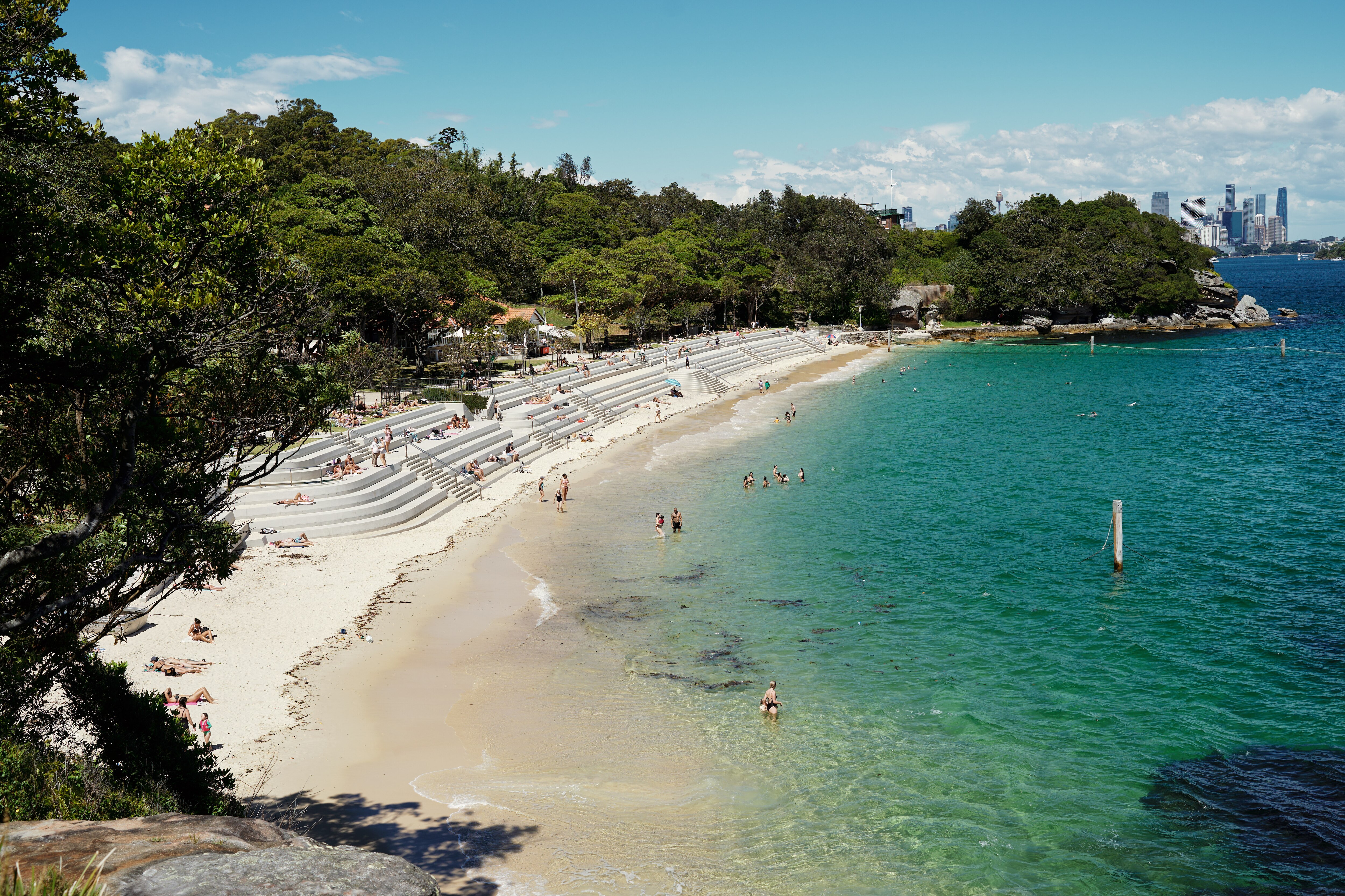A wide shot of people swimming at a beach and congregating on some sandy steps in the hot weather.