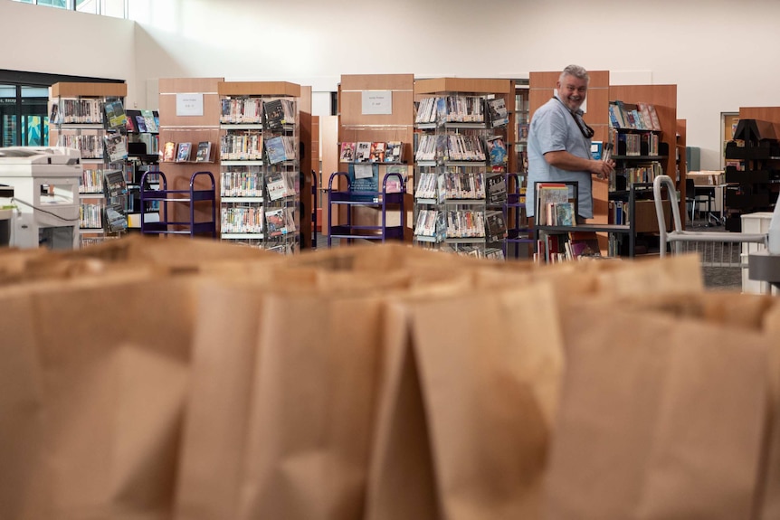 A table of brown paper bags with library shelves in the background