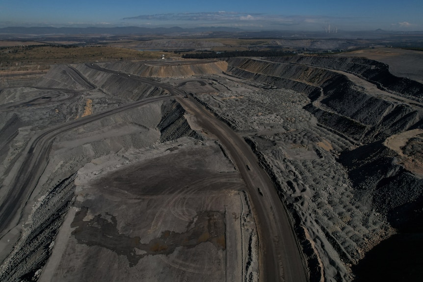A massive coal mine is cut into the ground in the Australian countryside.