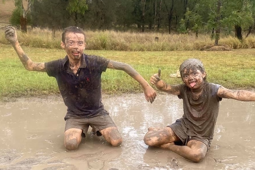 Two children play in a large mud puddle. Mud covers their clothes and faces.
