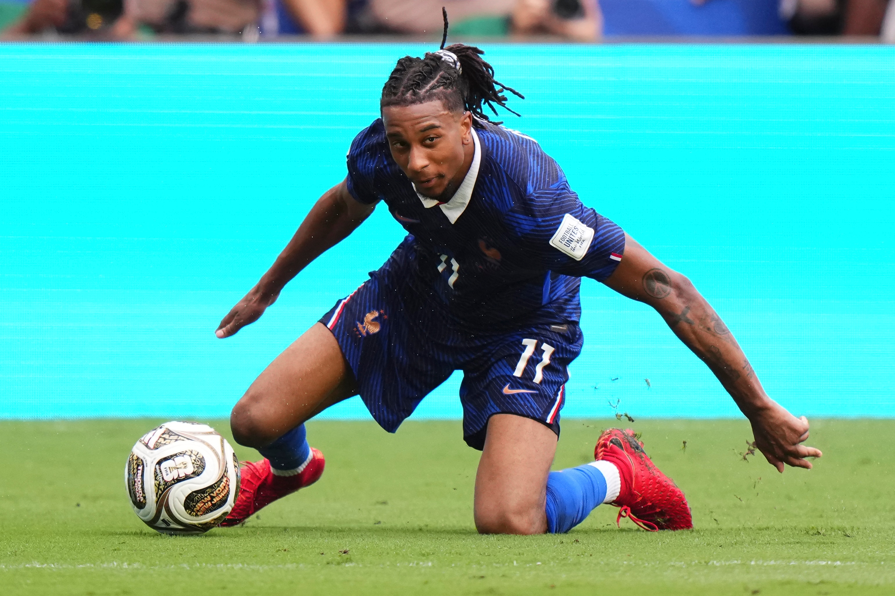 Michael Olise controls the ball while on his knees.