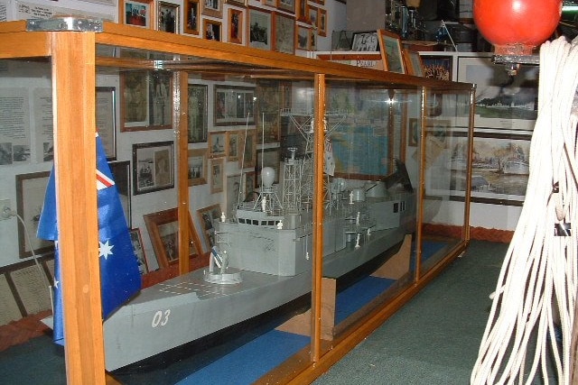 A grey model steel ship in a class container in a room with pictures all over the walls