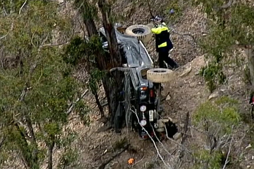 A 4WD rests on its side against a tree.