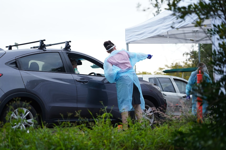 Health worker points as she speak to a driver at a COVID-19 testing drive-through 