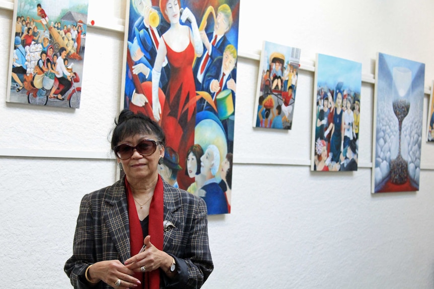 A woman with large sunglasses standing in front of colourful paintings