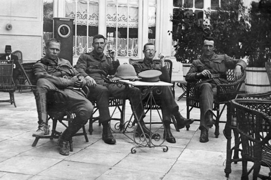 Group portrait of four Australian officers sitting on the terrace of a hotel.