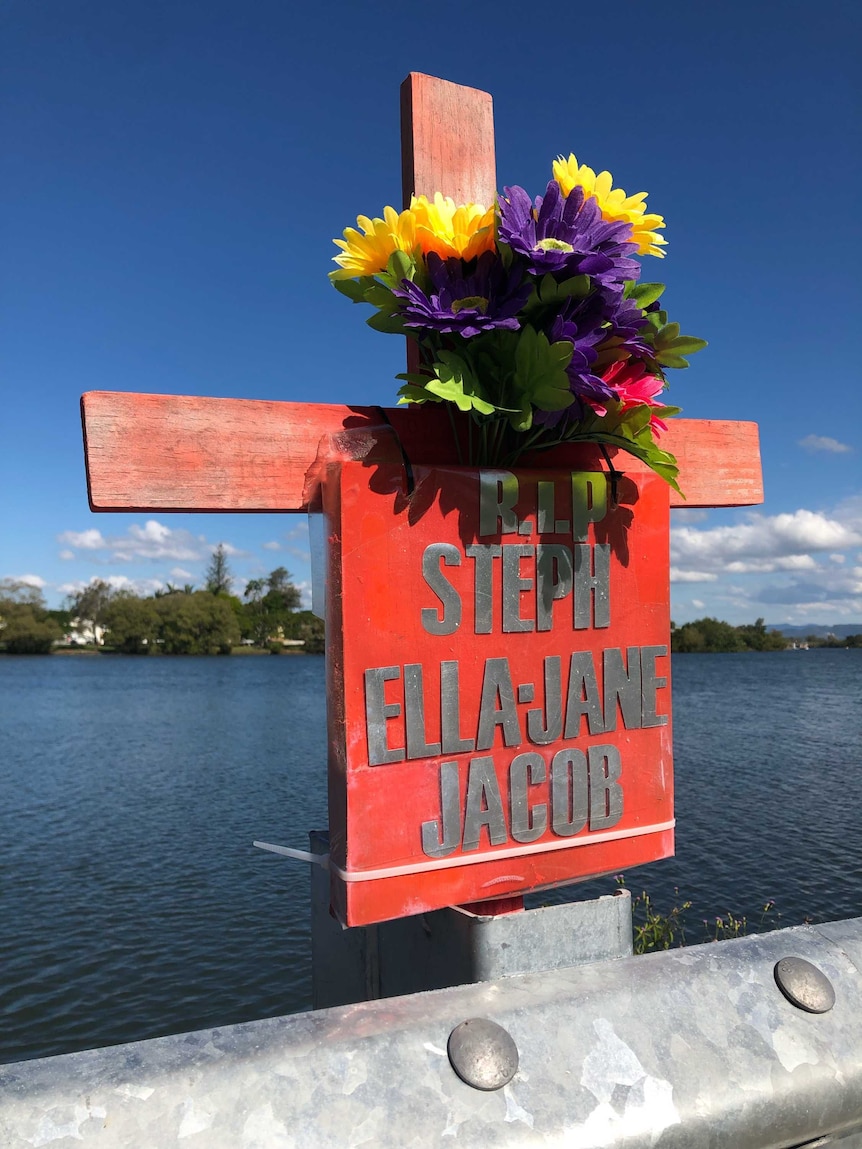 A wooden cross with yellow and purple plastic flowers and a sign saying 'R.I.P Steph Ella-Jane Jacob'.