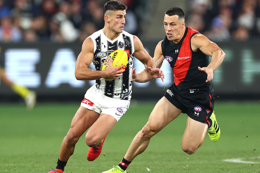 Nick Daicos holds the balls as Dylan Shiel looks to make a tackle from behind.