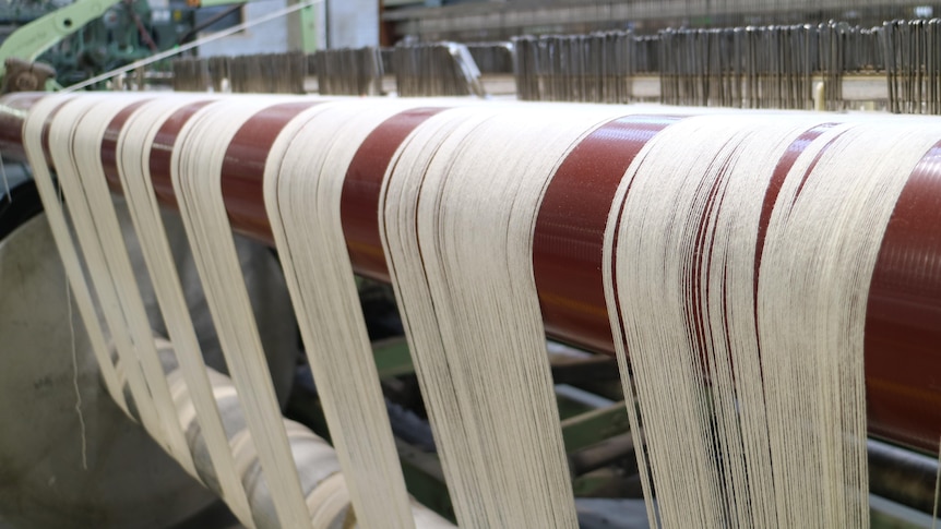 a textile machine inside a factory spins strips of white threads