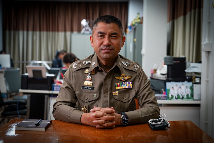 A close up of a man wearing a uniform and holding his hands infront of him on a desk.