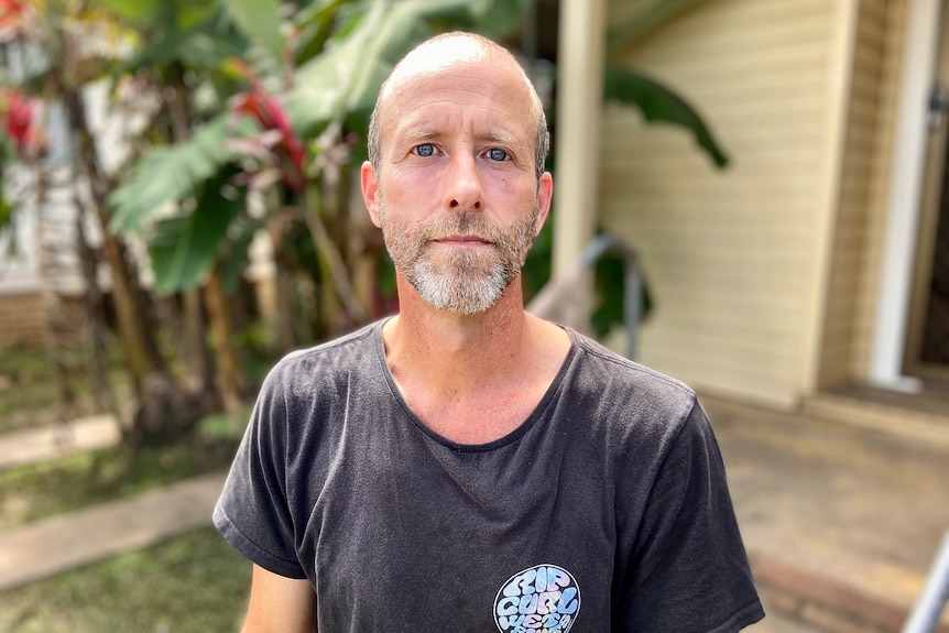 Man wearing a grey shirt standing outside a house.