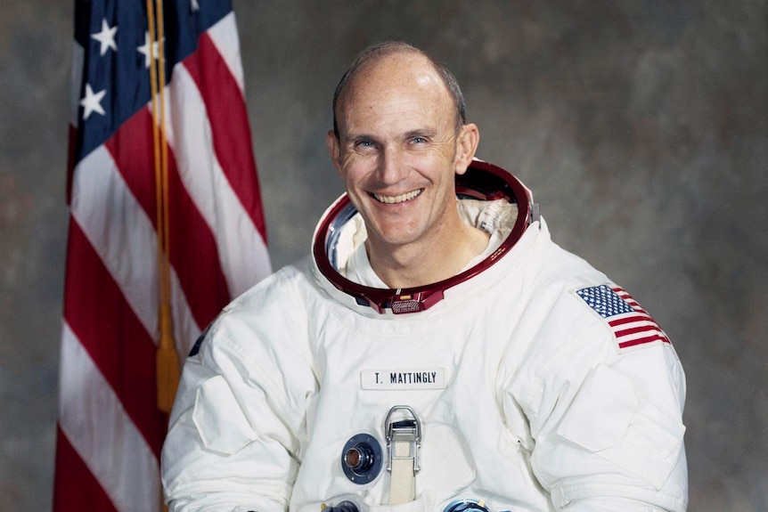 Man in an astronaut suit with both hands on a world globe, smiling to the camera