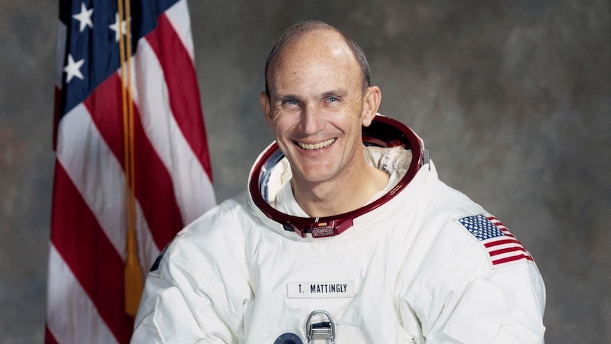 Man in an astronaut suit with both hands on a world globe, smiling to the camera