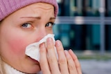 A woman blowing her nose with a tissue