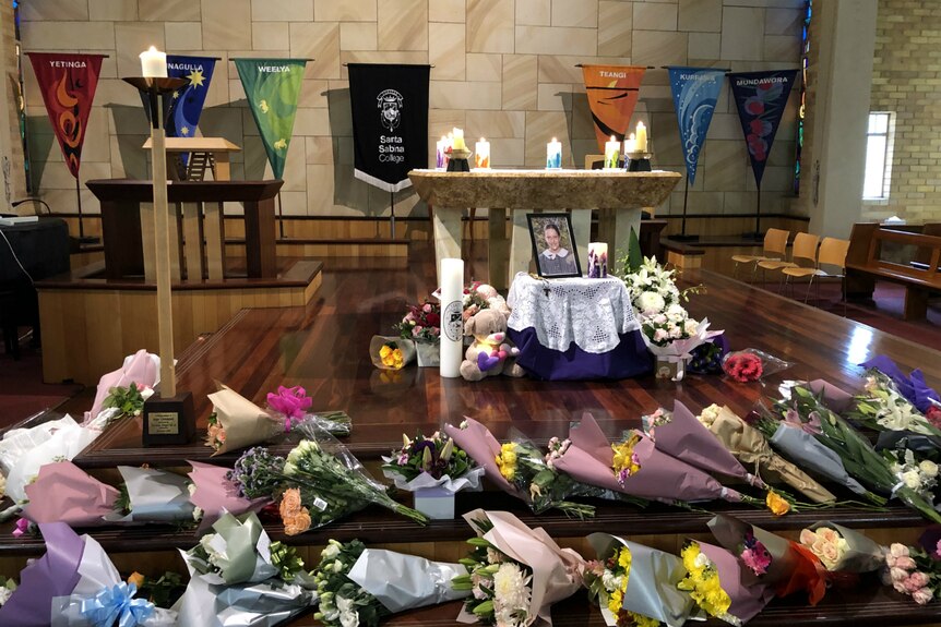 flowers and candles surrounding a memorial stand for a young girl