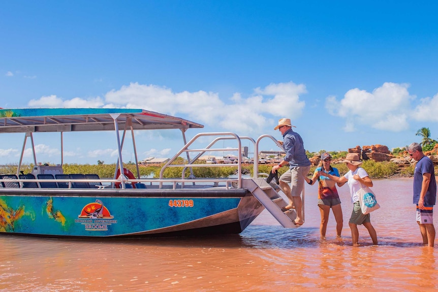 Tourists board a boat in water under a blue sky.