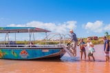 Tourists board a boat in water under a blue sky