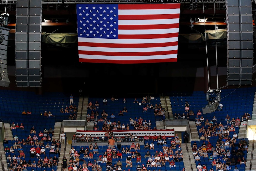 President Donald Trump supporters listen under a large American flag as Trump speaks during a campaign rally