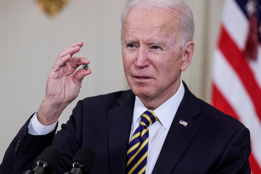 Joe Biden holds up a tiny little computer chip between his fingers 
