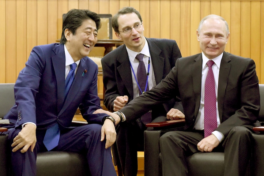 Władimir Putin śmieje się, trzymając za nadgarstek uśmiechniętego Shinzo Abe