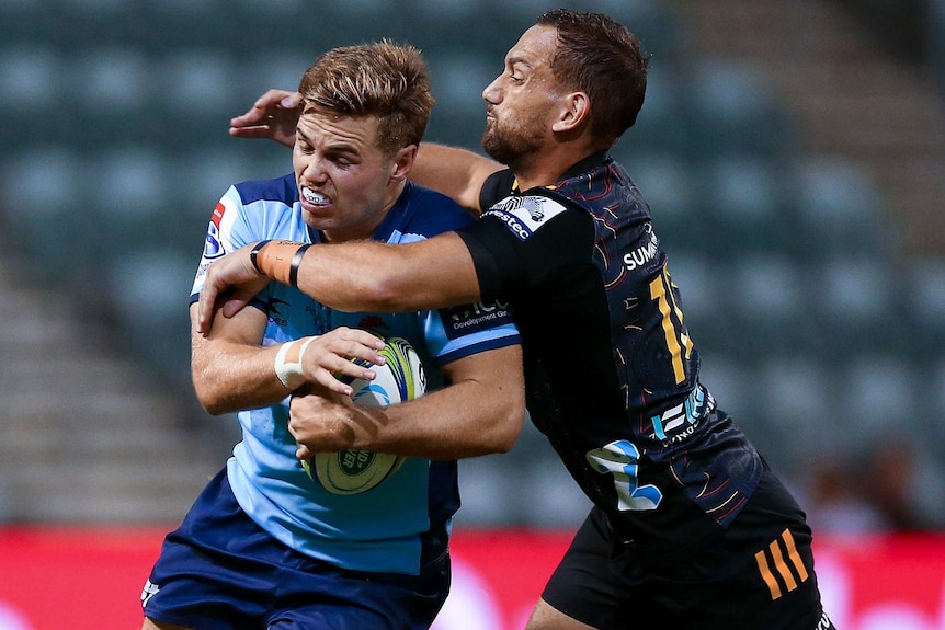 A NSW Waratahs player holds the ball as he is tackled around his upper body by a Chiefs opponent in Super Rugby.
