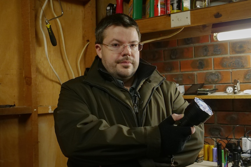 A man looking at the camera with a blank expression while holding a torch