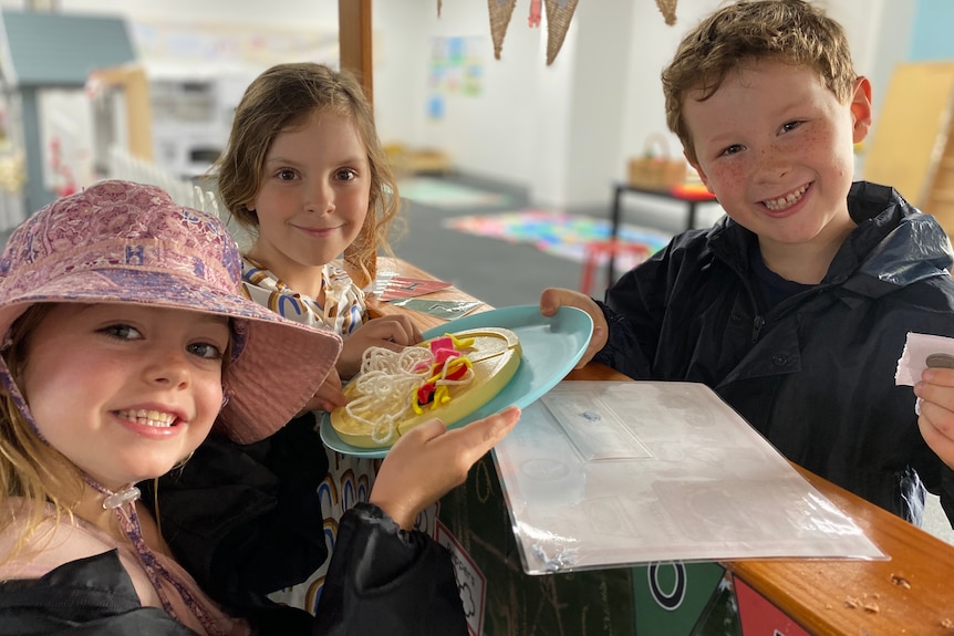 Kids hold a pretend plate of pasta and smile at camera.