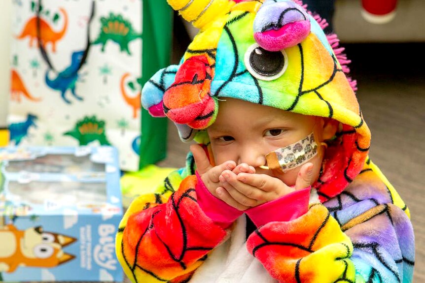 A child with an oxygen tube in his nose wears a onesy that looks like a rainbow unicorn